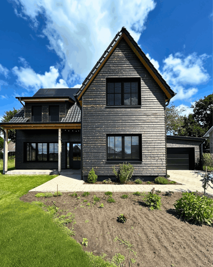 orderansicht eines fertiggestellten Einfamilienhauses mit dunkler Holzfassade, großem Fensterbereich und angebauter Garage.