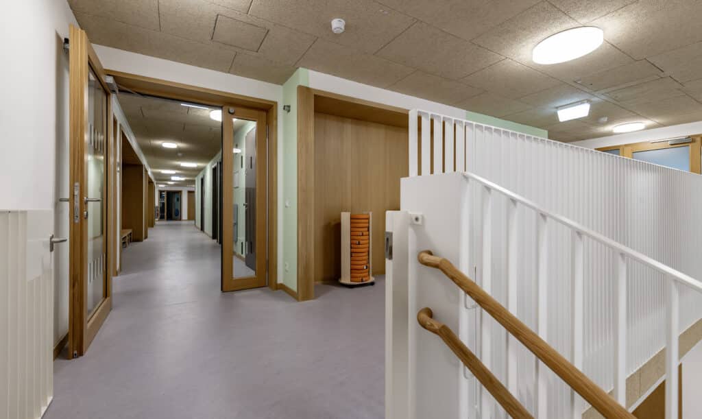 Flur einer Kindertagesstätte mit hellen Holztüren, Glasfeldern und weißen Geländern.