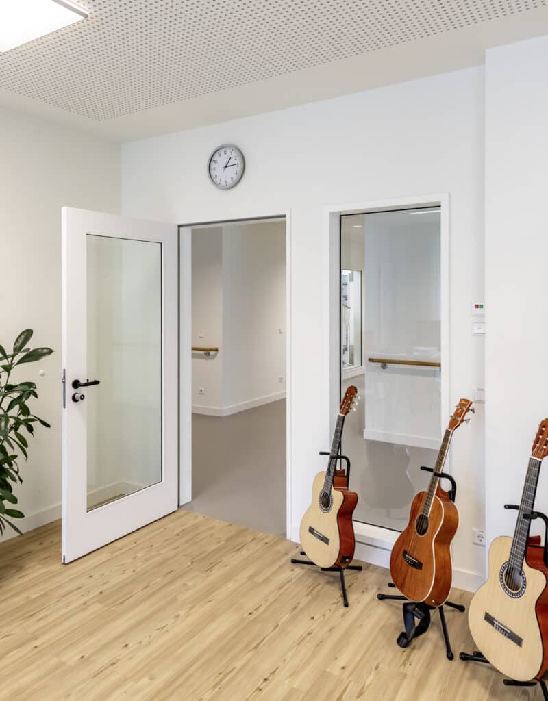 Drei Akustikgitarren stehen im Musikraum des Klinikums Wahrendorff, neben weißen Innentüren mit großen Glasfeldern.
