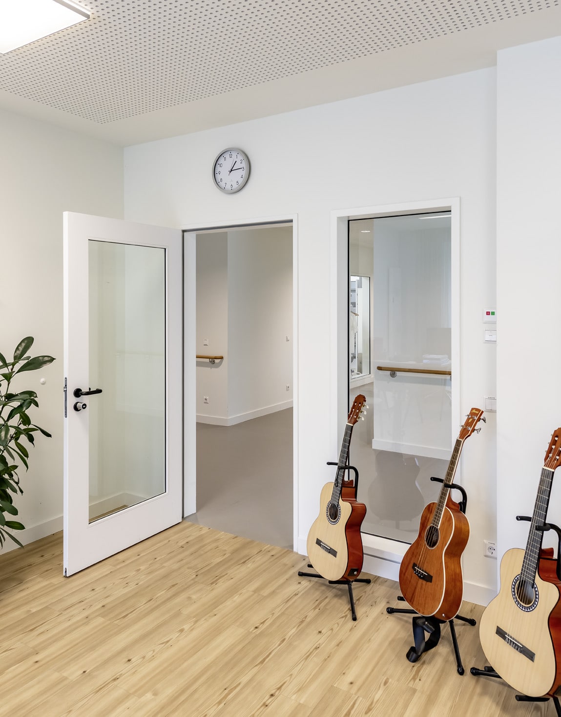 Drei Akustikgitarren stehen im Musikraum des Klinikums Wahrendorff, neben weißen Innentüren mit großen Glasfeldern.
