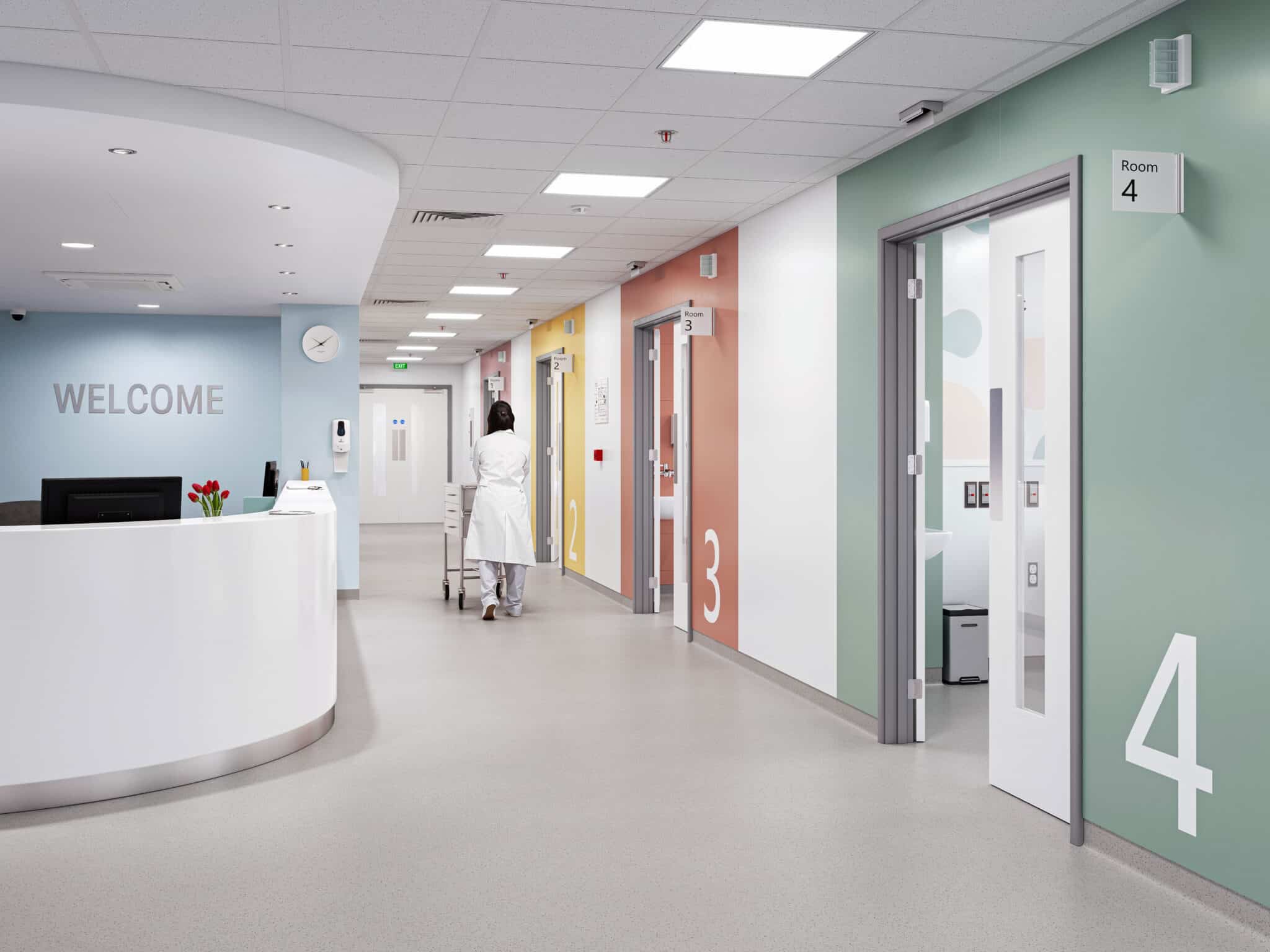Heller Krankenhausflur mit fugenarmem, rutschhemmendem Bodenbelag, farblich gestalteten Türen und moderner Empfangszone.