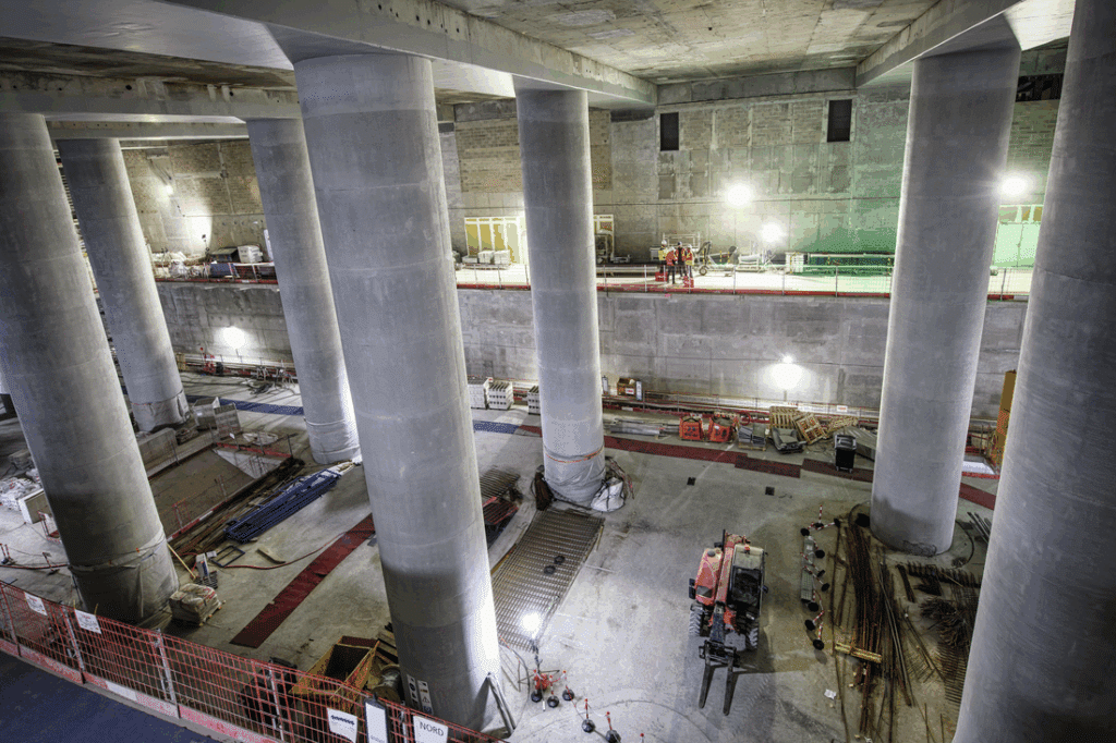 Großbaustelle mit massiven Betonstützen in unterirdischem Bauwerk.