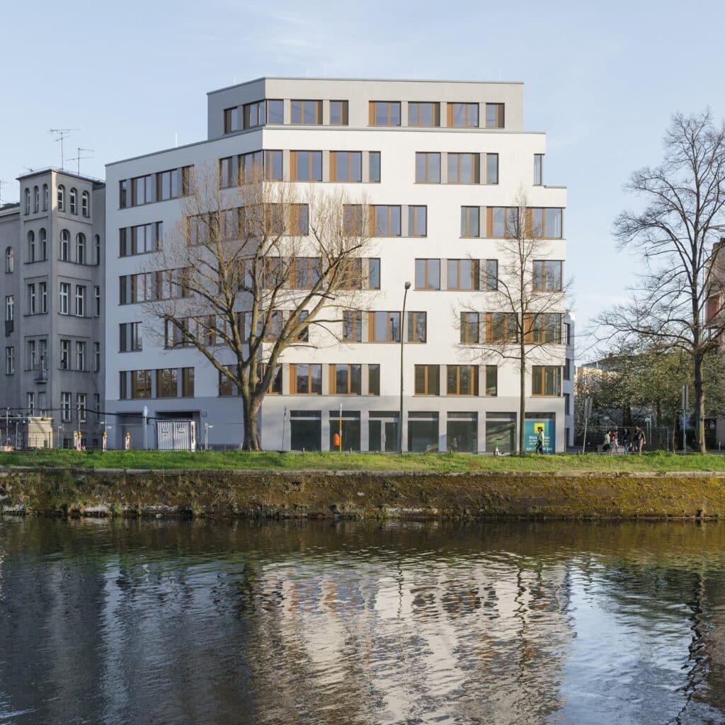 Bürogebäude mit gestaffelten Etagen und Uferblick, Spiegelung im Wasser sichtbar.