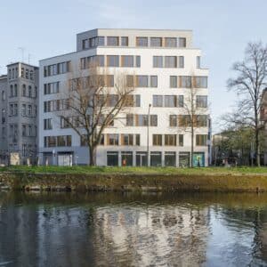 Bürogebäude mit gestaffelten Etagen und Uferblick, Spiegelung im Wasser sichtbar.