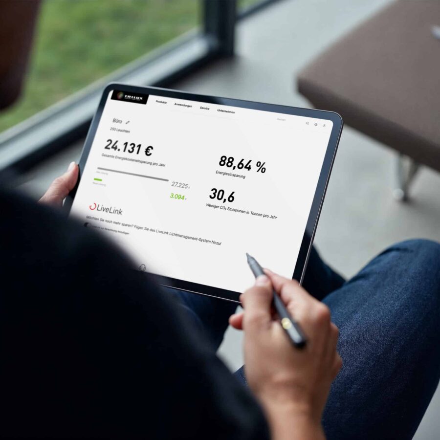 Person hält ein Tablet mit einer Energieberechnung zu Lichtsystemen, die Einsparungen und CO₂-Reduktion anzeigt.