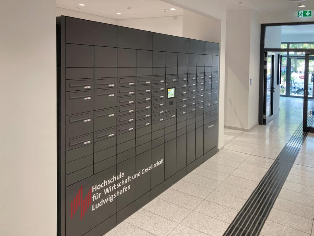 Komplett installierte RENZ-Paketkastenanlage in Schwarz mit integriertem Display und Logo der Hochschule für Wirtschaft und Gesellschaft Ludwigshafen.