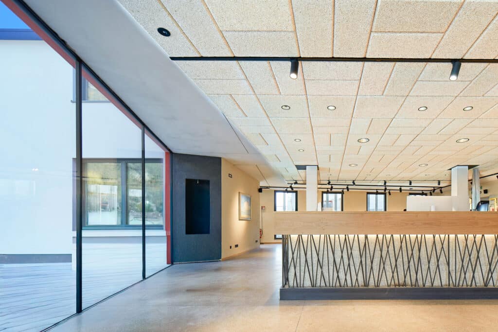 Moderner Innenraum mit hellen Akustikdeckenplatten, großer Glasfront und Empfangstheke mit strukturierter Verkleidung