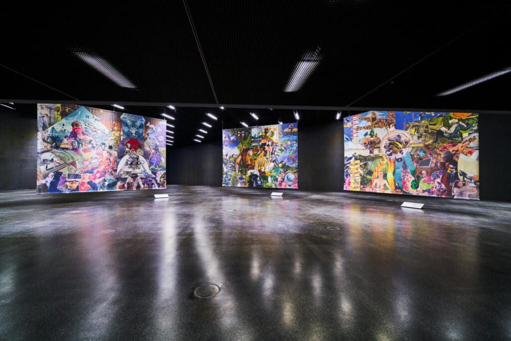 Großer, dunkler Ausstellungsraum mit glänzendem Boden und mehreren farbenintensiven Wandinstallationen, die unter Deckenstrahlern präsentiert werden.