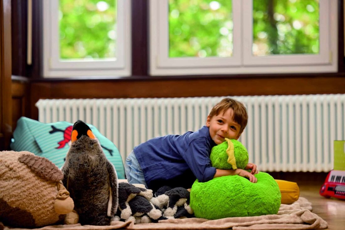 Junge spielt entspannt im Kinderzimmer vor einem weißen Zehnder Charleston Heizkörper, der für angenehme Wärme sorgt.