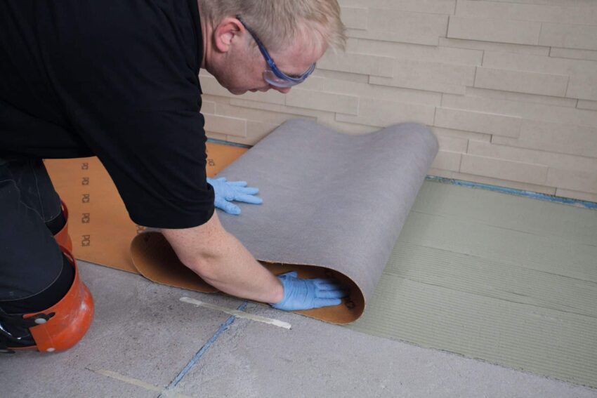 Handwerker rollt PCI-Entkopplungsmatte auf vorbereiteten Klebergrund aus, um Untergrundspannungen zu minimieren und ein gleichmäßiges Fugenbild zu erzielen.