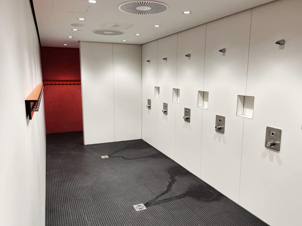 Moderne Duschanlage mit mehreren Duschplätzen und erkennbarer Wasserableitung im Bodenbereich.