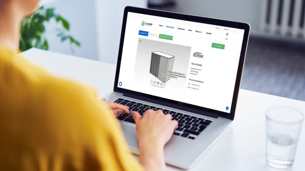 Person arbeitet an einem Laptop, auf dessen Bildschirm ein 3D-Modell einer Kermi-Wärmepumpe im QualityBIM-Portal angezeigt wird; die Webseite zeigt technische Informationen, Firmenkontakt und Downloadoptionen.