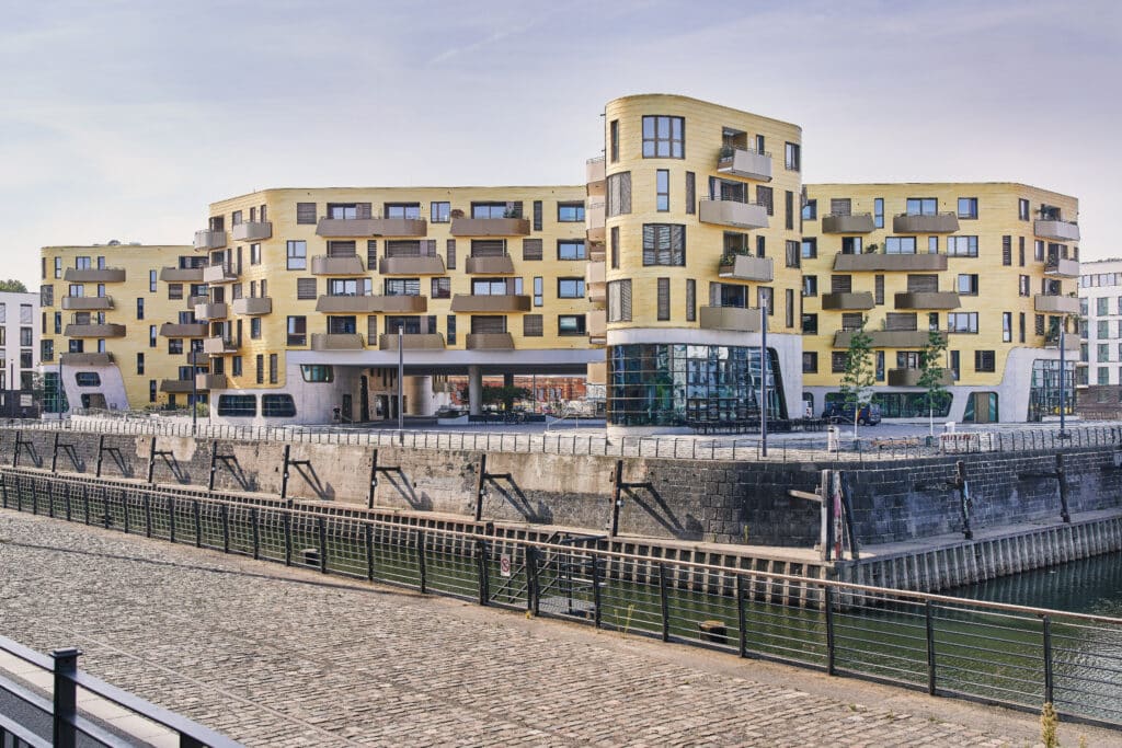 Gesamtansicht des PANDiON DOXX in Mainz mit gelber Fassade, Erkerformen und großflächiger Verglasung direkt am Hafenbecken.
