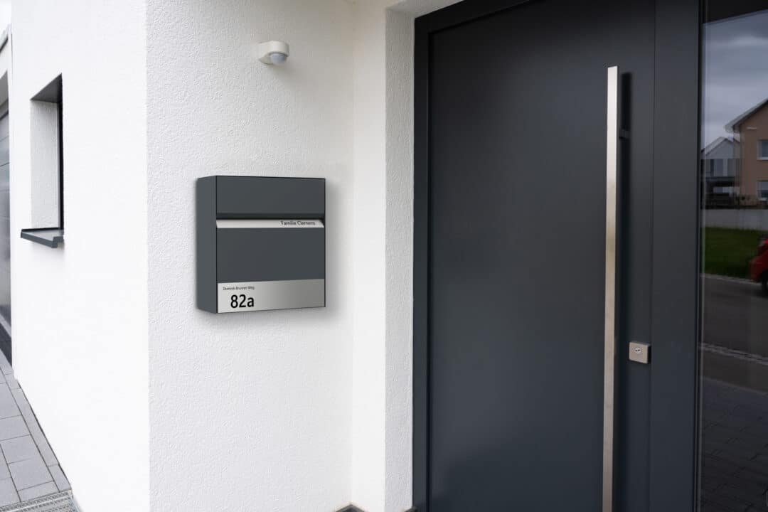 Moderner Wandbriefkasten mit integrierter Hausnummer neben einer Haustür an der Fassade eines Wohnhauses.