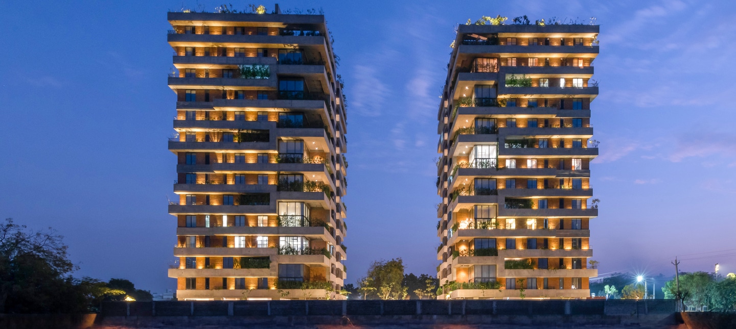 Zwei moderne Wohnhochhäuser des Projekts Skydeck Select in Indien, beleuchtet in der Abenddämmerung, mit großen Balkonen und begrünten Fassaden.