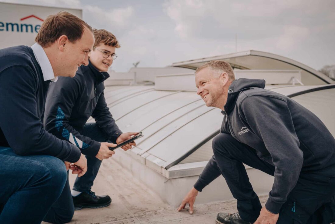 Drei Fachleute bei einer Dachinspektion auf einem Flachdach mit Lichtkuppeln im Gespräch.