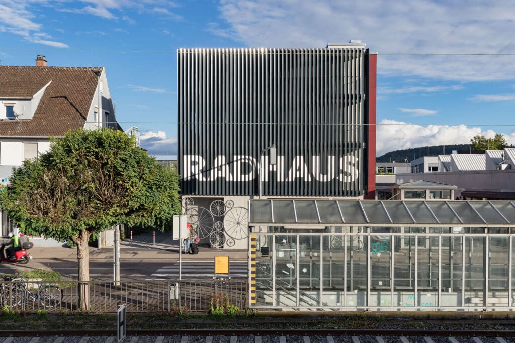 Fassade des Radhaus Schorndorf mit vertikalen Lamellen und großem Schriftzug RADHAUS, im Vordergrund Bahnhofsgelände und Baum