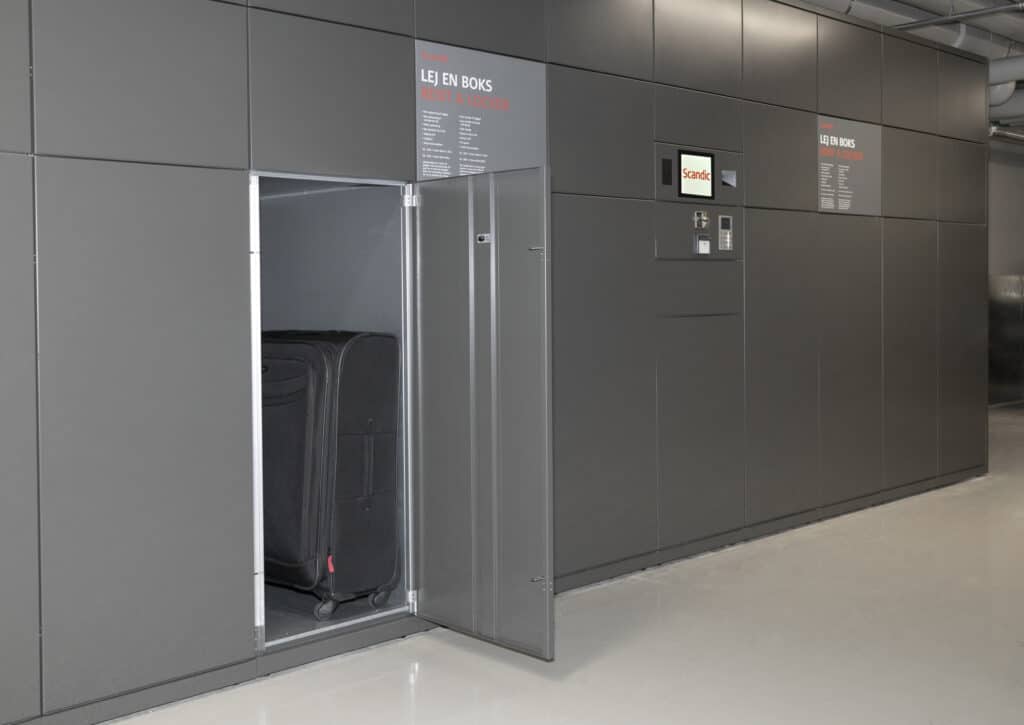 Großes graues Gepäckschließfach im Scandic Spectrum Hotel, geöffnet mit sichtbarem schwarzen Rollkoffer