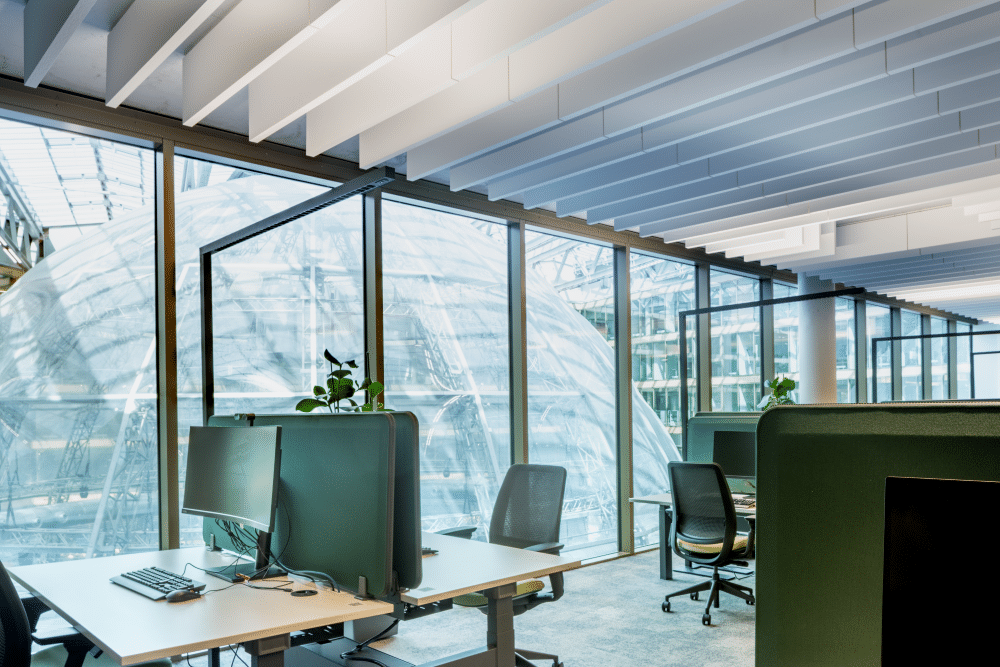 Arbeitsplatz mit Blick auf Glasfassade und akustisch wirksamen Deckenelementen.