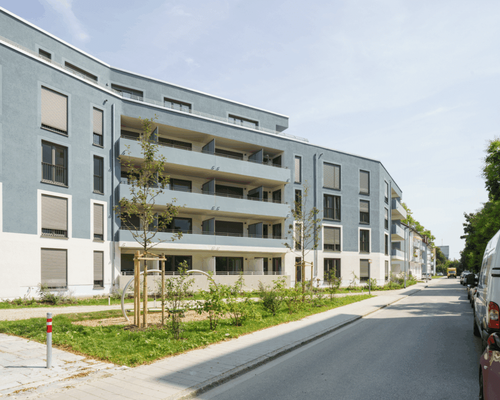 Moderne Wohnanlage mit blau-grauer Fassade, großzügigen Balkonen und begrüntem Vorgarten in städtischer Umgebung.