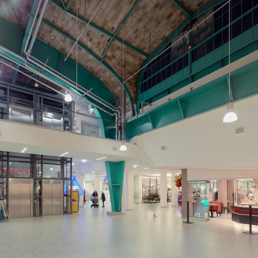 Modern gestaltete Passage mit Backsteingewölbe, grünen Stahlträgern und heller Ladenfläche im Erdgeschoss.