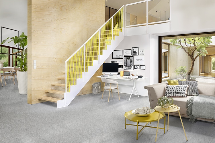 Helle Design-Holztreppe mit weißem Stahlwangensystem und gelbem Geländer in einem freundlichen Wohn- und Arbeitsbereich mit Homeoffice.