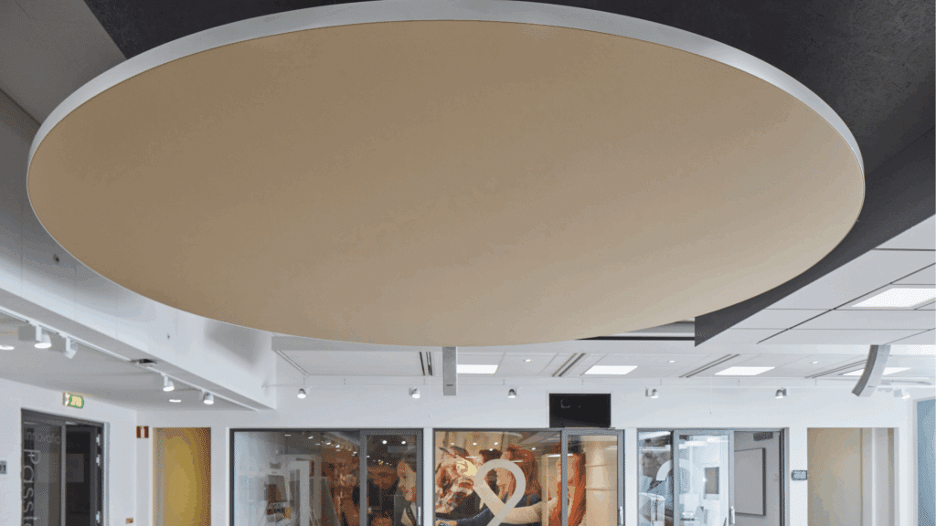 Innenaufnahme eines Ausstellungsraums mit großem, runden, beigen Deckenelement als Akustik- und Designelement, vor weißer und schwarzer Deckenstruktur.