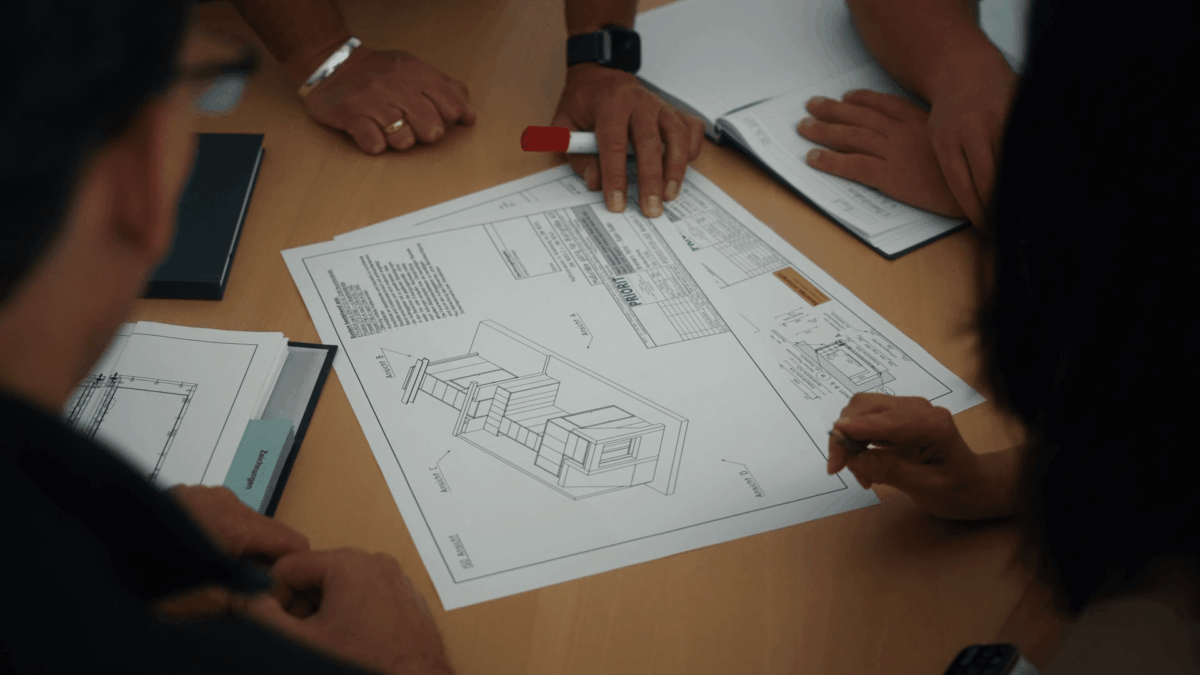 Mehrere Personen sitzen an einem Tisch und besprechen technische Zeichnungen zu einem PRIORIT-Projekt für Brandschutzlösungen.