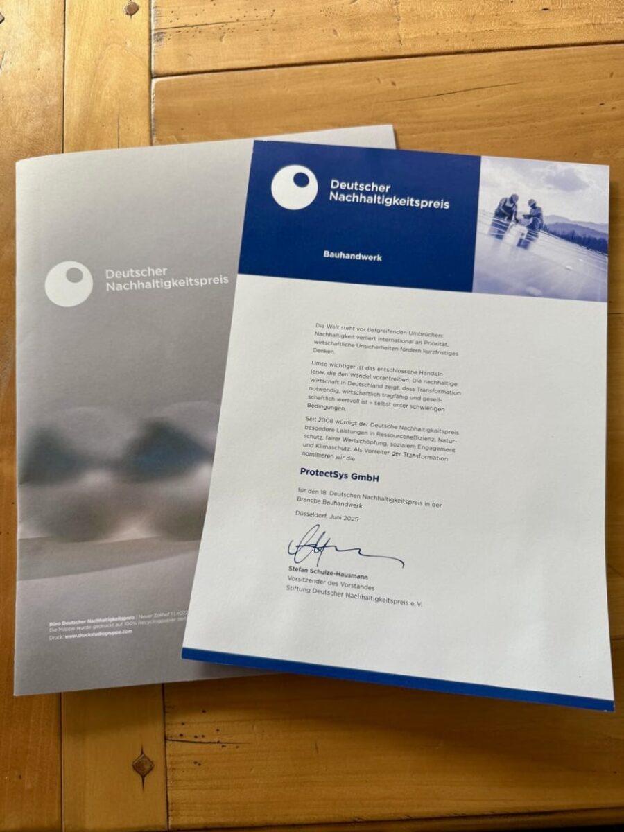 Auf einem Holztisch liegen das Anschreiben und die Unterlagen zur Nominierung der ProtectSys GmbH für den Deutschen Nachhaltigkeitspreis 2025 in der Kategorie Bauhandwerk.