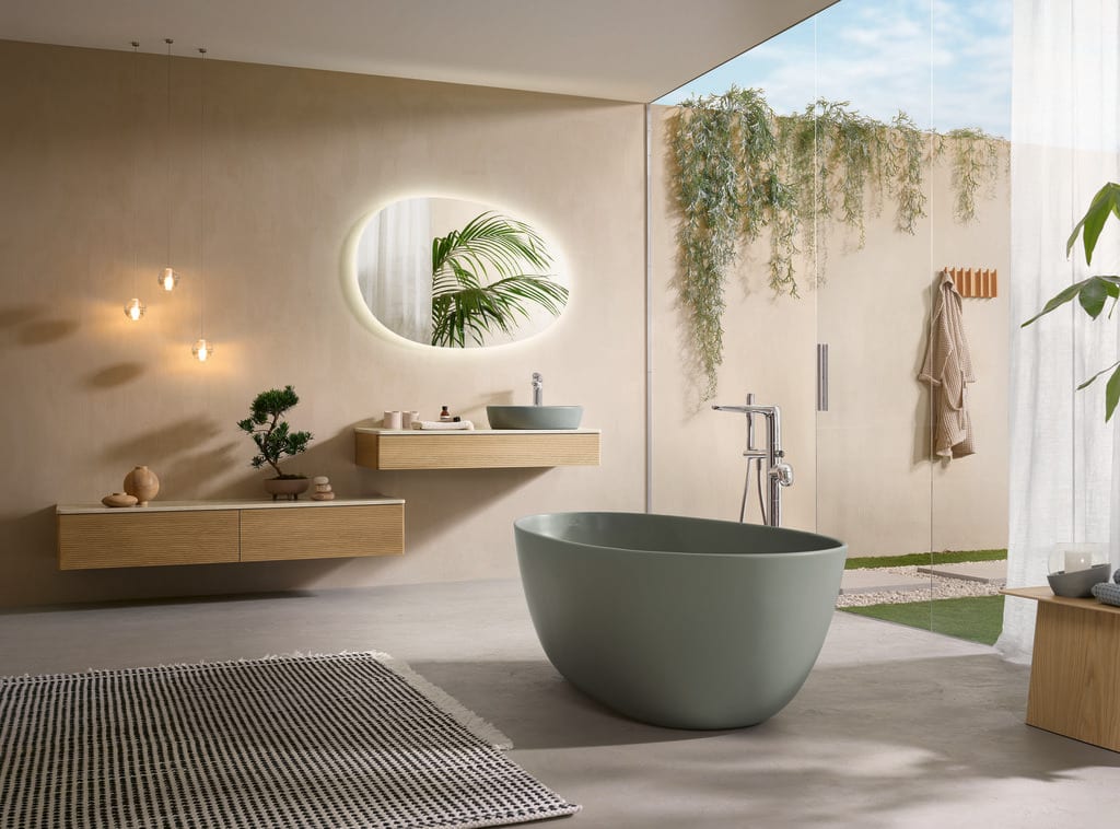 Modernes Badezimmer mit freistehender Antao-Badewanne in Salbeigrün, Waschtisch mit Aufsatzschale und großem Fenster mit Blick ins Grüne.