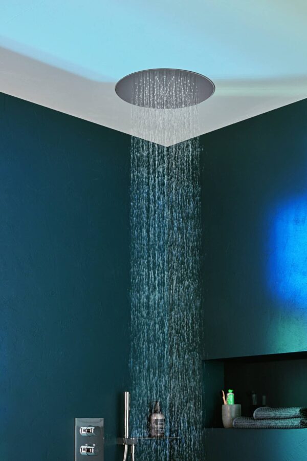 Runde, in die Decke eingelassene Regendusche, aus der ein kräftiger Wasserfallstrahl in ein modernes Bad mit dunkelgrünen Wänden und farbigen Lichtreflexen fällt.
