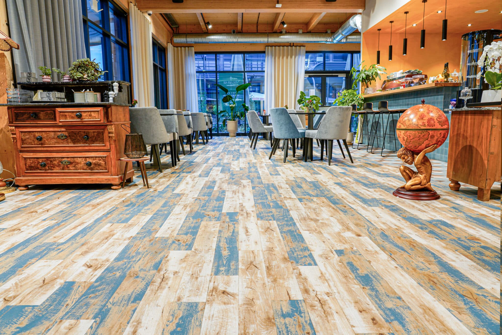 Restaurant mit auffälligem Holzoptikboden in Blau- und Naturtönen, gemütlicher Einrichtung und warmem Lichtkonzept.