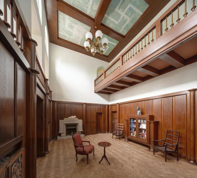 Großer historischer Innenraum mit Holzvertäfelung, Galeriegeschoss und dekorativer Decke in einer restaurierten Villa.