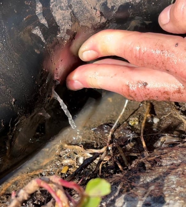 Hand drückt auf eine beschädigte Kunststoffoberfläche, aus der seitlich Wasser austritt; Nahaufnahme einer Leckage.