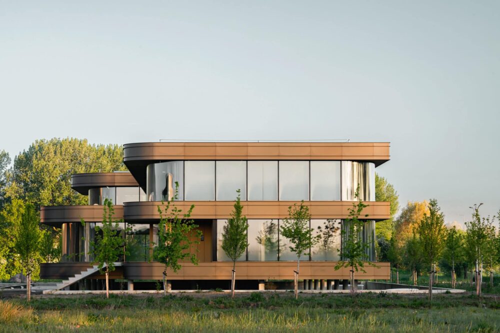 Seitliche Ansicht des Omega-Bürogebäudes mit geschwungener Fassade, großen Glasfronten und nachhaltiger Architektur im Grünen.