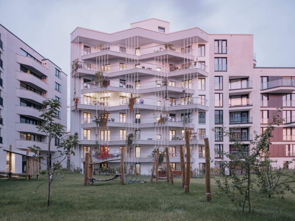 Außenansicht des Baugruppenhauses „Heimatmole“ in Hamburg mit markanter Fassadengeometrie, begrünten Balkonen und Gemeinschaftsgarten im Vordergrund.