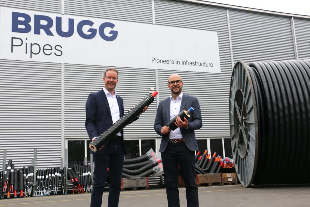 Zwei Vertreter von BRUGG Pipes präsentieren innovative Rohrsysteme vor dem Firmengebäude mit großem Kabeltrommel-System im Hintergrund.