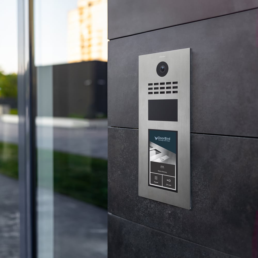 Edelstahl-Türstation DoorBird D31x an moderner Gebäudefassade mit Kamera, Lautsprecher und Touchdisplay.