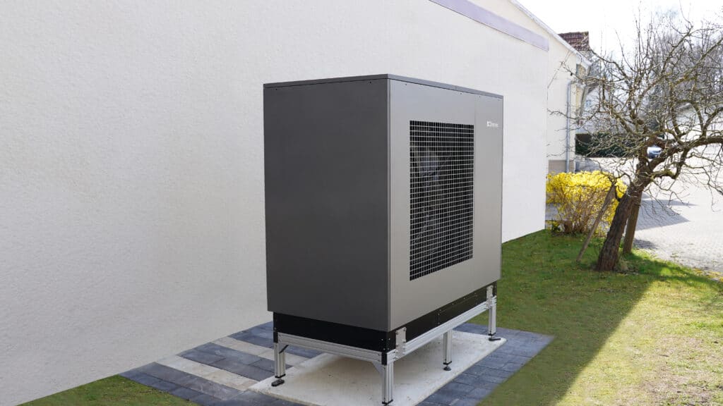 Außenansicht einer installierten Wärmepumpe Dimplex System M Compact auf Fundamentplatten an einer Hauswand.