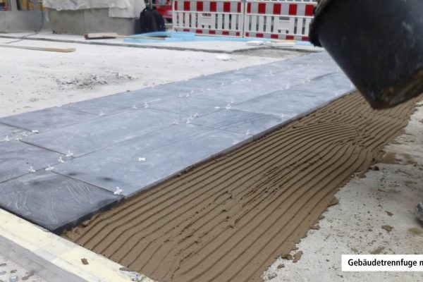 Fachgerechte Verlegung von Bodenplatten an einer Gebäudetrennfuge mit Fugenprofil auf der Baustelle.