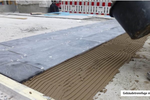 Fachgerechte Verlegung von Bodenplatten an einer Gebäudetrennfuge mit Fugenprofil auf der Baustelle.