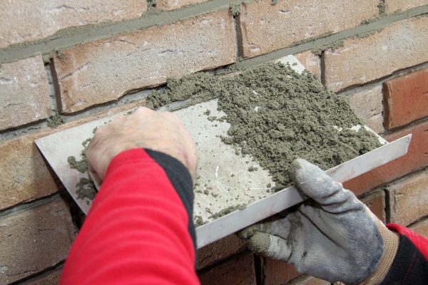 Handwerker trägt Fugenmörtel händisch mit einer Fugenkelle präzise auf die Fugen einer Ziegelwand auf.