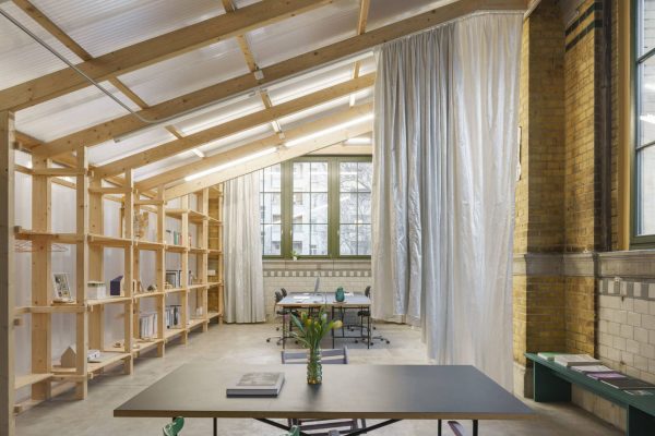 Moderner Arbeitsraum in einer historischen Industriehalle mit Holzregalen und Vorhängen als gezielte Interventionen.