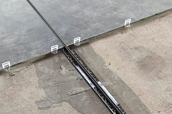 Verlegung grauer Bodenfliesen mit Nivelliersystem und einer präzisen Feldbegrenzungsfuge Großformat im Belag.