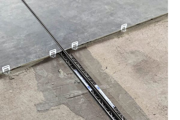 Verlegung grauer Bodenfliesen mit Nivelliersystem und einer präzisen Feldbegrenzungsfuge Großformat im Belag.