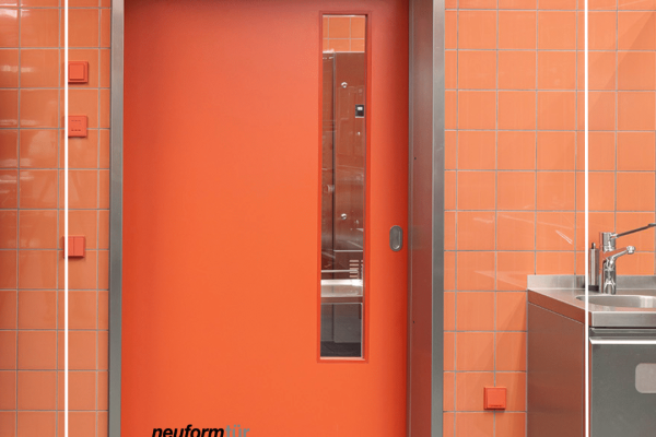 Rotes Framic-Element mit Stahlzarge und Sichtfenster vor einer Wand aus orangefarbenen Fliesen.