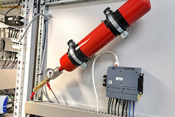 Rote Preveneos Löschmittelflasche mit Manometer an einer Schaltschranktür neben einem Steuermodul.