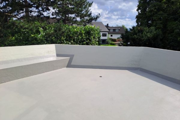 Verarbeitung der grauen MOGAT LIQUID SOLO 1K Flüssigabdichtung auf einer Terrasse mit weißer Brüstungswand.