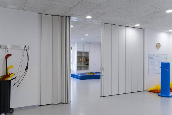 Helle Sporthalle einer Grundschule bietet flexible Nutzungsmöglichkeiten durch Trennwandsysteme in schlichtem Weiß.