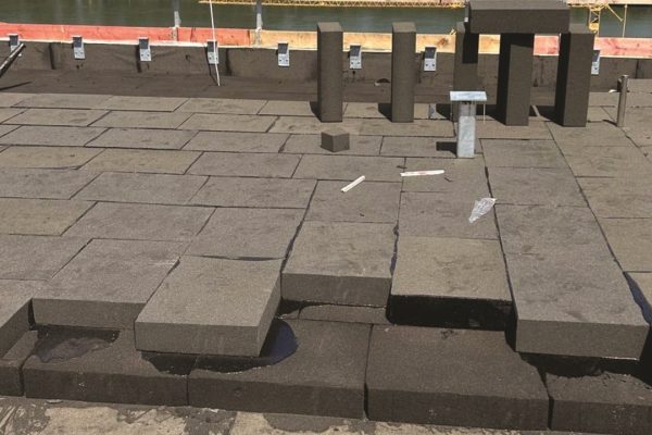 Verlegung einer grauen Gefälledämmung auf einem Flachdach mit Blick auf einen Fluss zur sicheren Entwässerung.